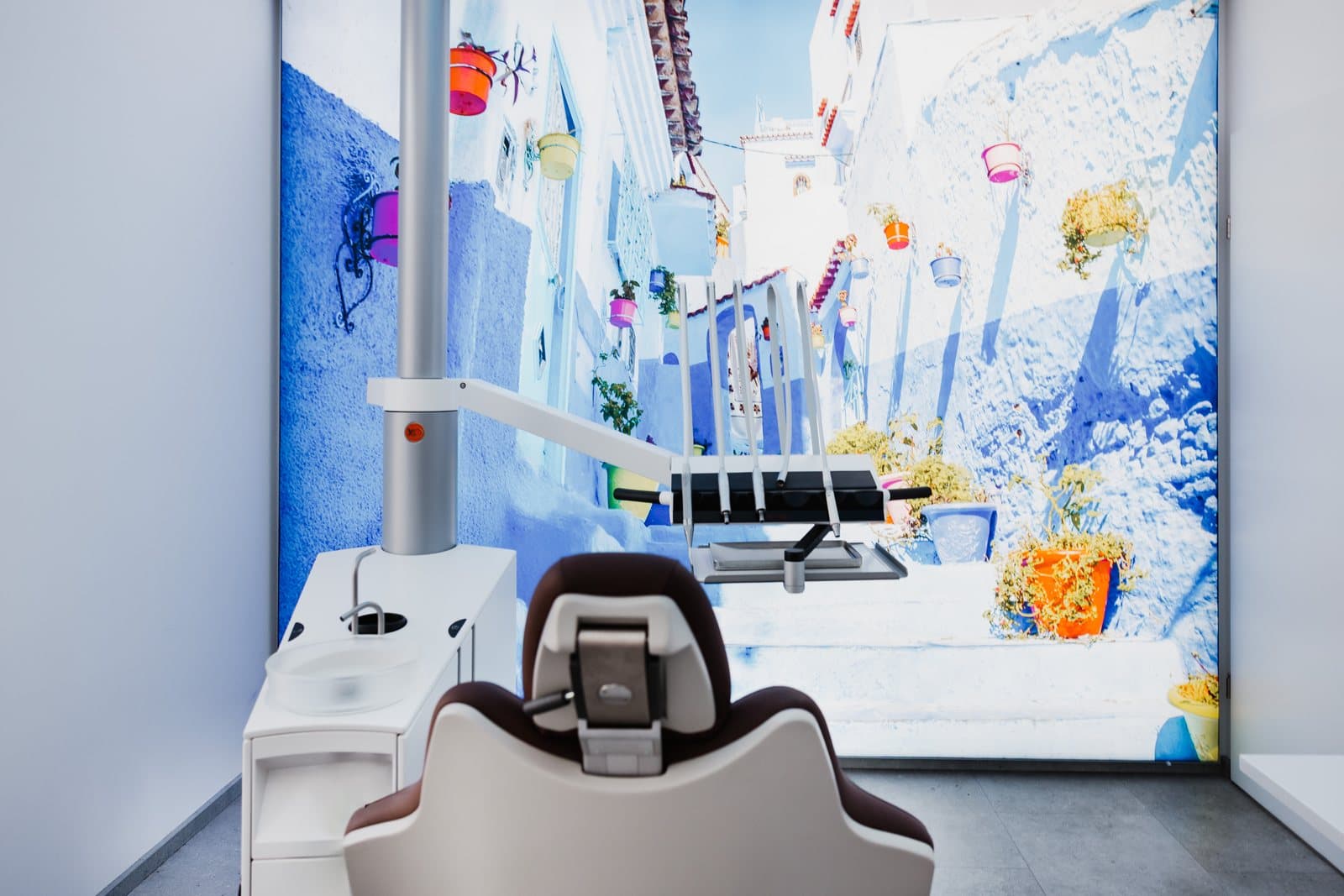 Wandbild einer blau gestrichenen Gasse mit Blumentöpfen im Behandlungszimmer der Praxis in Gallneukirchen